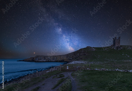 Vibrant Milky Way composite image over landscape of Dunstanburgh Castle on Northumberland coastline in England