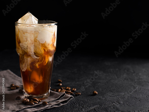 tall glass cold brew coffee with ice and milk on black or dark background