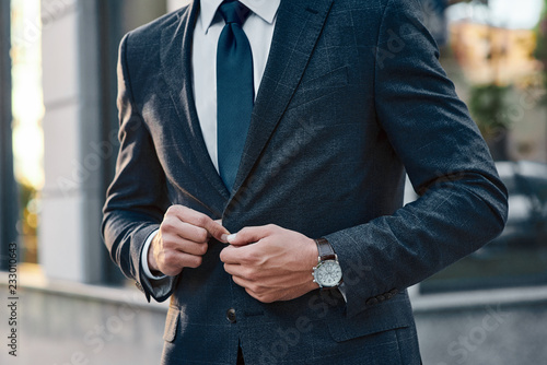 A young businessman fastens a suit jacket. He has on his hands an expensive watch.