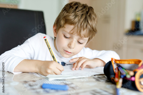 Tired little kid boy at home making homework at the morning before the school starts. Little child doing excercise, indoors. Elementary school and education.