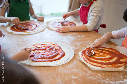 Children's hands make pizza - spread tomato sauce on the base.