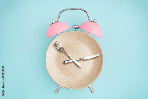 Alarm clock and plate with cutlery . Concept of intermittent fasting, lunchtime, diet and weight loss