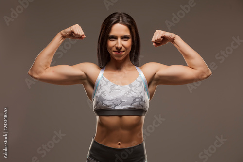 Pretty muscular young woman posing on gray background