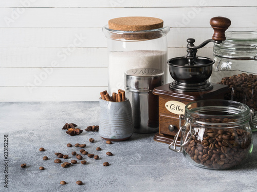 Various ingredients for making coffee, Glass jars with coffee beans, sugar, coffee grinder and milkman with cinnamon and anise stars on gray background. Copy space