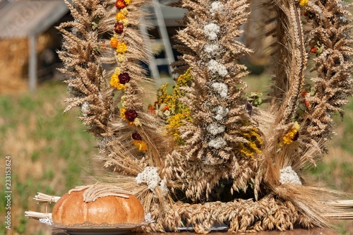 Tradycyjny wieniec dożynkowy z położonym obok chlebem i wplecionymi kwiatami.