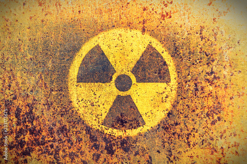 Round yellow radioactive (ionizing radiation) danger symbol painted on a massive rusty metal wall with rustic grunge texture background. Washed fading yellow rust color toned.