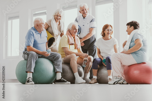 Low angle on smiling senior people on balls after gymnastic classes at sport club