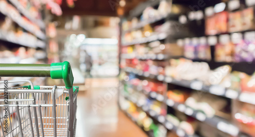 Empty green supermarket shopping cart with abstract blur grocery store aisle defocused background