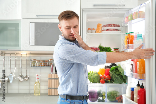 Man feeling bad smell from stale products in refrigerator at home
