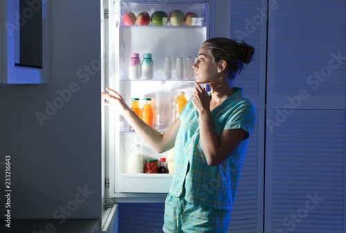 Woman choosing food from refrigerator in kitchen at night