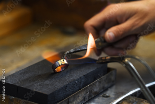 goldsmith hand is glowing a golden wedding ring with a gas flame, copy space in the dark background