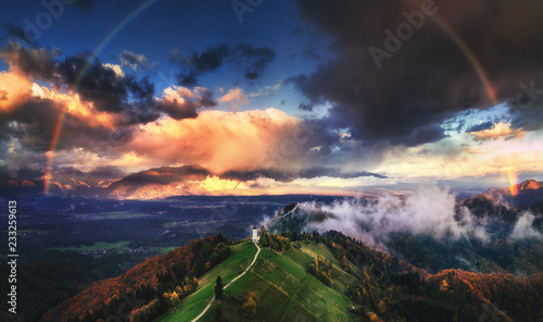 Jamnik, Slovenia - Aerial view of rainbow over the church of St. Primoz in Slovenia near Jamnik with beautiful clouds and Julian Alps at background.