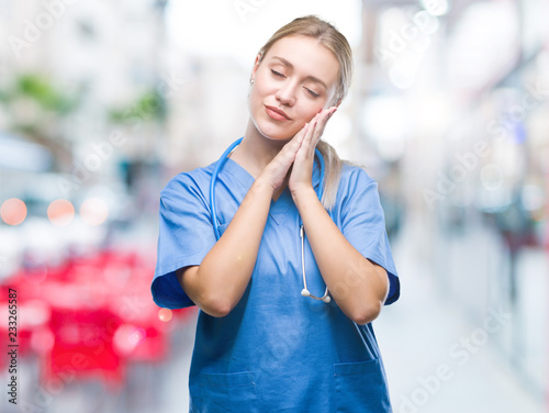 Young blonde surgeon doctor woman over isolated background sleeping tired dreaming and posing with hands together while smiling with closed eyes.