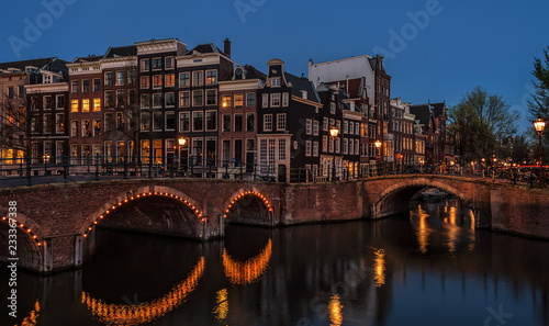 Night view of Amsterdam cityscape with canal, bridge and medieval houses in the evening twilight illuminated. Amsterdam, Netherlands