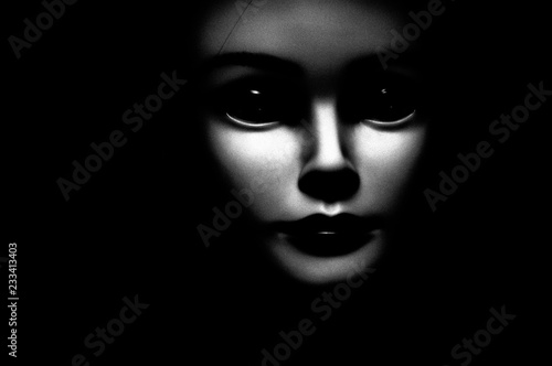 Close up of a spooky looking black eyed child looking passed viewer, featuring oversized black eyes, pale skin and black background.