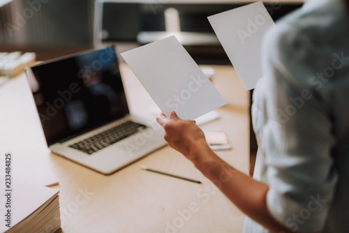 Close up of white templates for design in female hands. Woman standing near office table with laptop