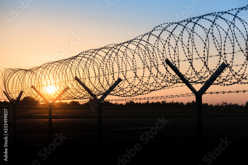 Silhouette of a barbed wire fence steel jail with the sunset in the background