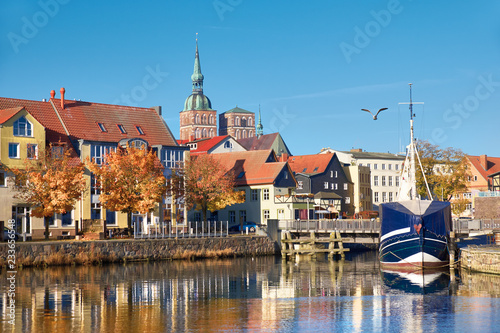Docked sail boats and houses reflecting in channel with brick towers of Stralsund, Germany