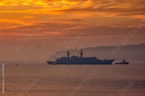 Military Battleship using tugs go to the port at the sunrise time