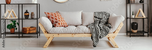 Light grey sofa with patterned pillow and black and white blanket in real photo of scandi living room interior with metal racks with decor