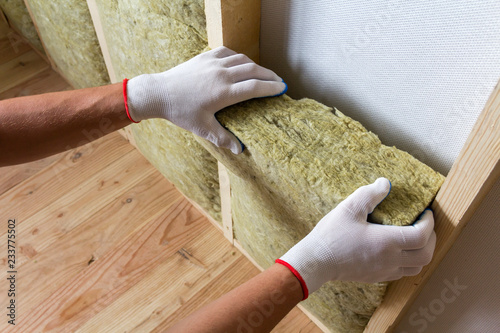 Close-up of worker hands in white gloves insulating rock wool insulation staff in wooden frame for future walls for cold barrier. Comfortable warm home, economy, construction and renovation concept.