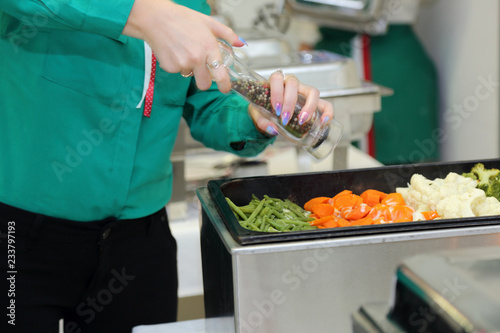 Kelnerka posypuje pieprzem gotowane warzywa na kateringu.