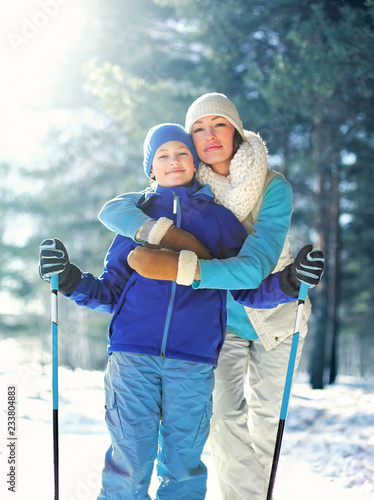 Portrait happy smiling mother hugging child with ski in winter cold forest