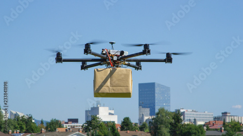 CLOSE UP: UAV drone delivery delivering big brown post package into urban city