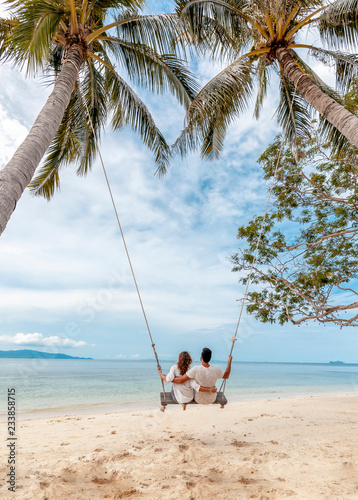 Young couple swinging on a swing on paradise tropical beach, honeymoon, vacation, travel concept