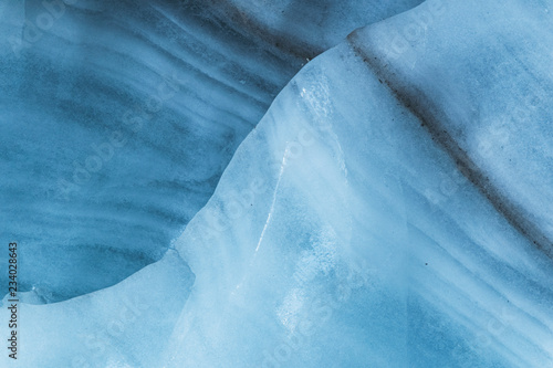 Close-up wall of a centuries-old glacier with a structure of stripes and bubbles. Ice blue light texture