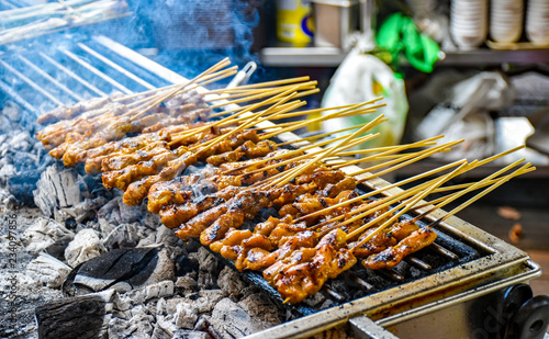 Satay skewers with chicken meat are prepared on a charcoal grill. Smoke rises from the grill.