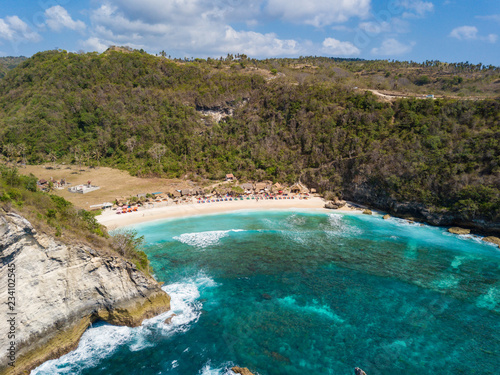 Aerial view to beautiful Atuh beach with buildings, sunbeds and hindu temple. Turquoise ocean water. Photo from drone. Nusa Penida, Bali, Indonesia
