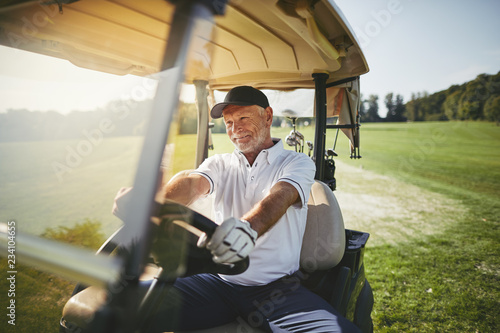 Smiling senior man driving his golf cart on a fairway