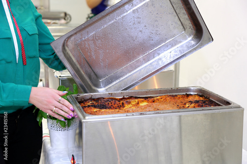 Catering, kelnerka odsłania stalową pokrywę patelni z gotowym jedzeniem.