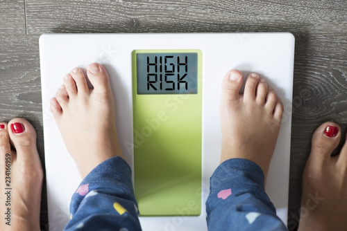 Childhood obesity high risk for health problems with child’s feet on weight scale under the supervision of his mother 