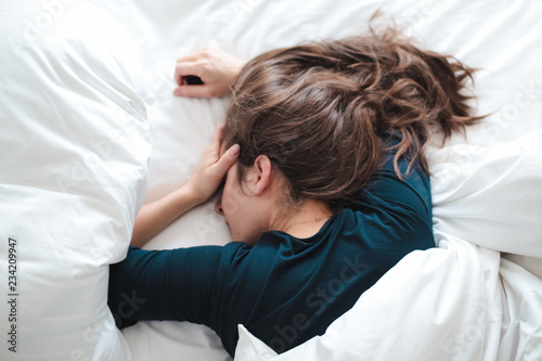 young woman in bed holding her head