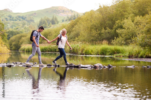 Couple Crossing River Whilst Hiking In UK Lake District