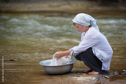 A girl in a long village vintage clothes sitting on the Bank of the river and washes clothes in the basin.