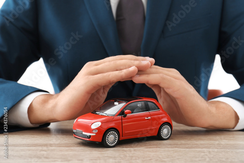 Insurance agent covering toy car on table, focus on hands