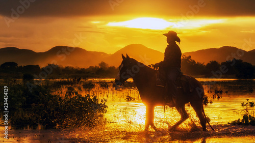 Silhouette the cowboy riding on a mountain with an yellow sky; Concept of friendly and of summer vacation.