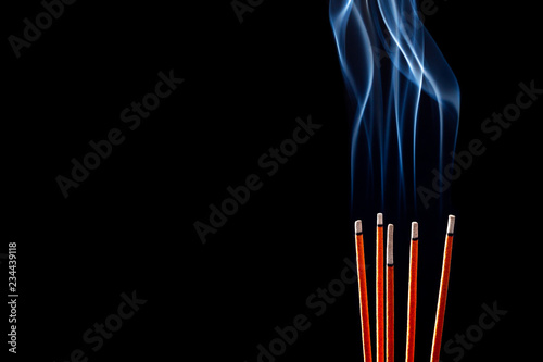 Closeup of calmly burning incense sticks with blue fume on black background