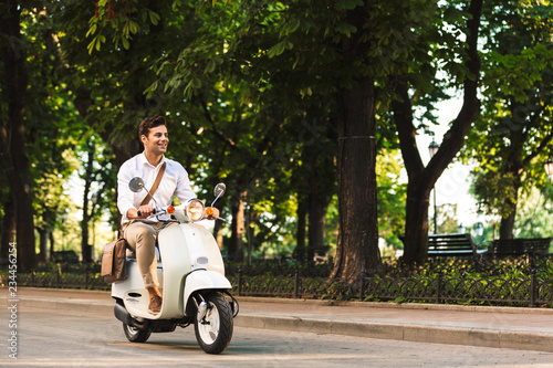 Young business man walking outdoors on scooter.