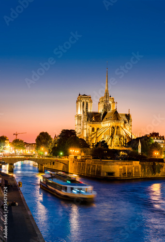 Notre Dame de Paris with cruise ship on Seine river at night in Paris, France,vertical