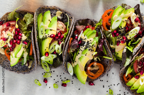 Gluten-free vegan tacos from black bean with tomato and avocado salad with tahini sauce and pomegranate seeds. healthy fast food for the whole family or party