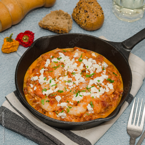 National greek dish saganaki with shrimps. Shrimp saganaki with tomato and feta cheese in a pan. Homemade shrimp and tomato sauce with feta in pan on napkin top. 