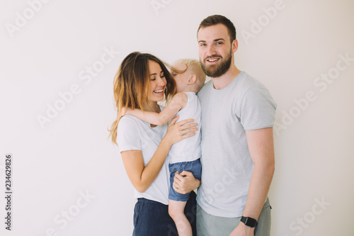Happy young family with little son standing together in casuals near the empty wall - indoors ..