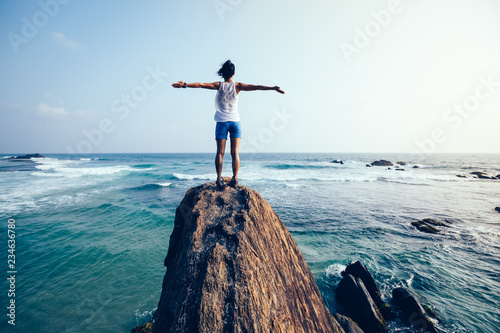 Freedom young woman outstretched arms on seaside rock cliff edge