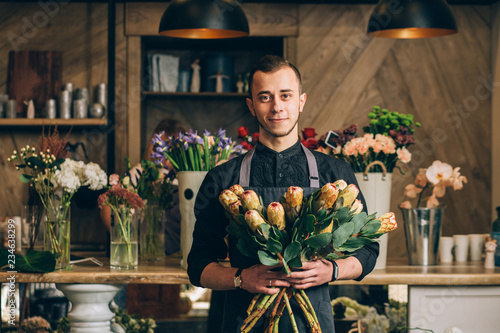 Man florist holding a protea flowers arrangements in modern interior floral shop. Small business, welcoming concept.