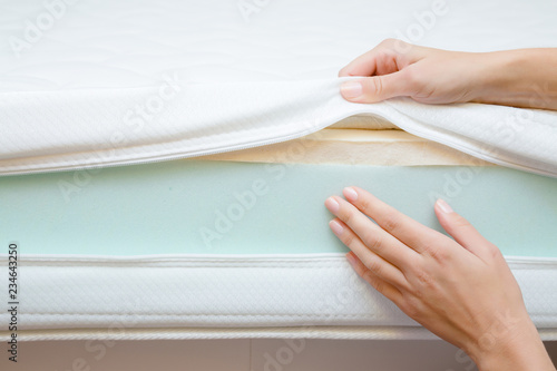 Woman's hands touching different layers of new mattress. Checking hardness and softness. Choice of the best type and quality. Front view. Close up.