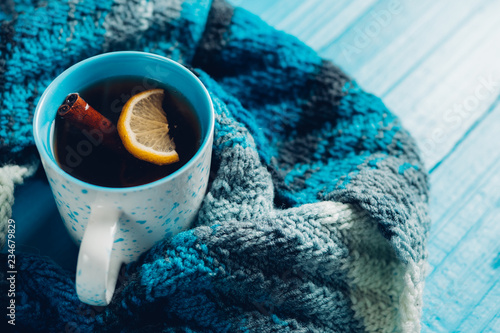 A mug of hot tea with cinnamon on a blue background with a scarf